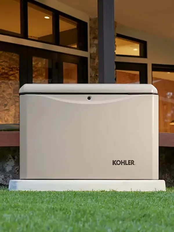 A Kohler Home Generator is shown in a beige case in front of a modern home.