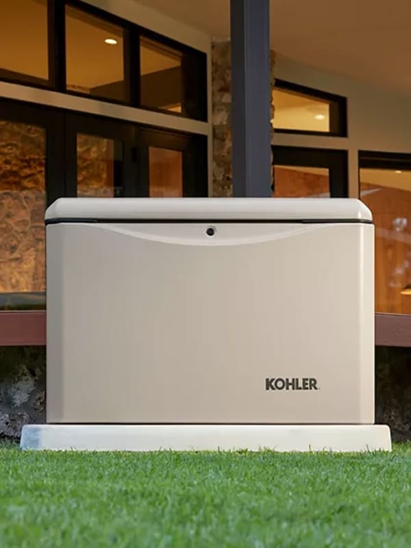 A Kohler Home Generator is shown in a beige case in front of a modern home.